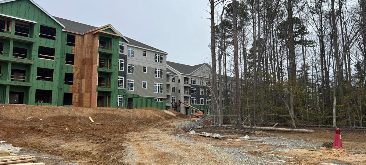 Construction site with multi-story apartment buildings framed in green sheathing and exposed wood structure under overcast sky.