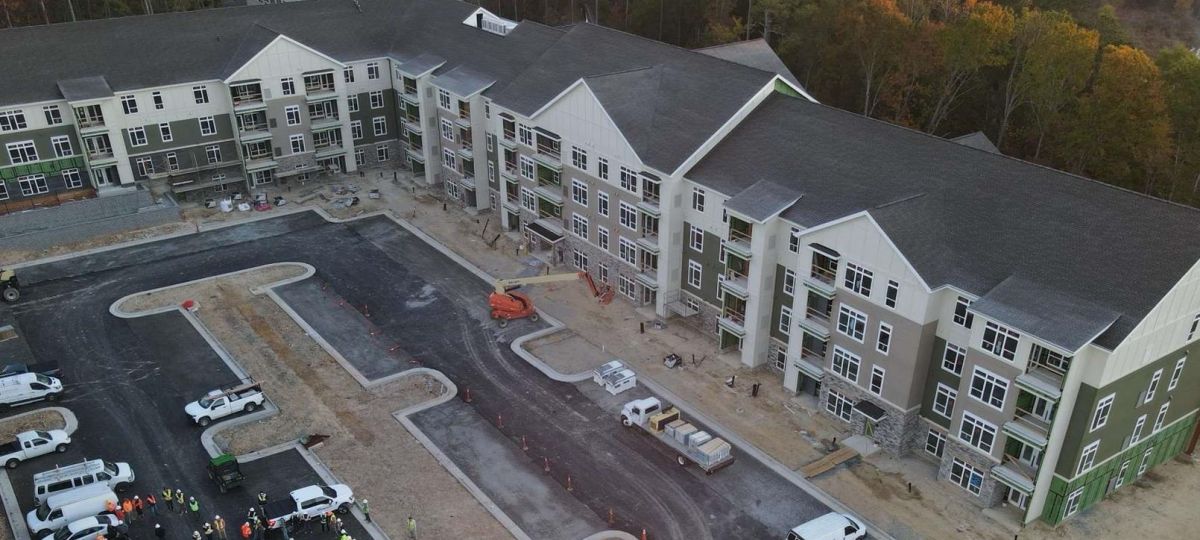 Aerial view of newly built apartment complex with parking lot, construction crew, and landscaped surroundings.