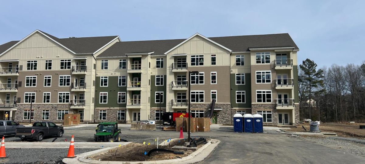 Front view of completed multi-story apartment building with balconies and construction materials in foreground.