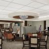 Spacious senior living dining room with booths, fireplace, modern chandeliers, and residents enjoying conversation.